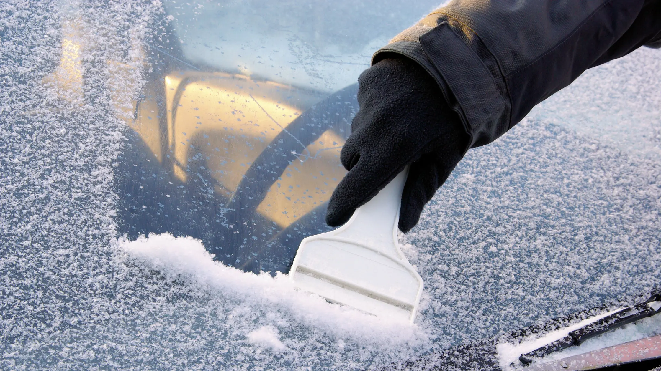 En hand ses skrapa en bilruta full med is och snö.